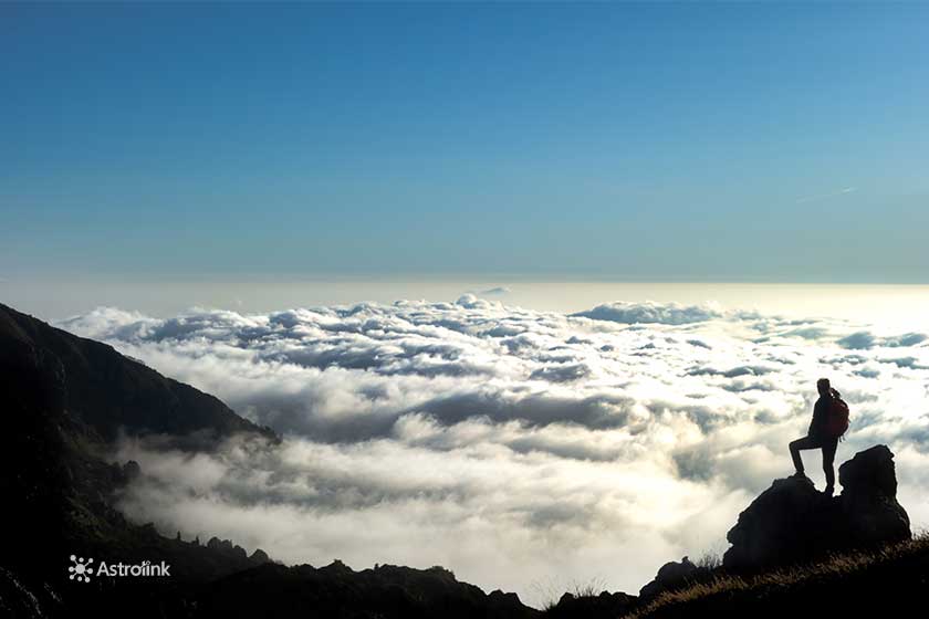 silhueta de uma pessoa parada no topo de uma montanha, observando as nuvens